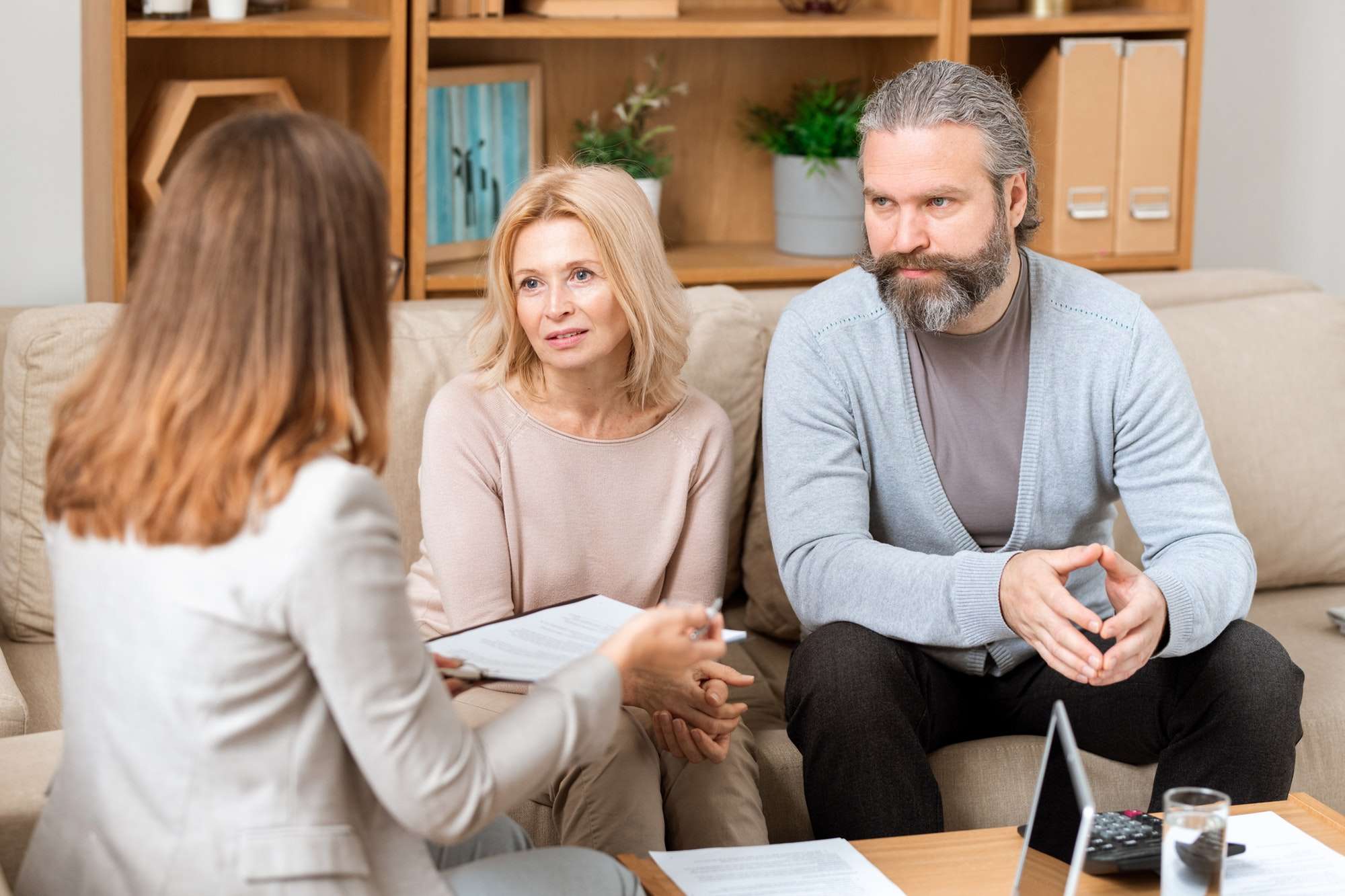 Mature man and his wife sitting on sofa and consulting with real estate agent